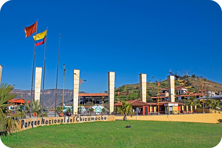 Puerta de acceso al Parque Nacional Chicamocha, con señalización del parque y visitantes entrando mientras disfrutan del paisaje.