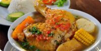 Sancocho de gallina presentado en un plato hondo, con gallina, papa, plátano y yuca, decorado con hojas de cilantro fresco.