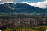 Formaciones rocosas de Suesca con montañas majestuosas al fondo y vegetación verde en primer plano.